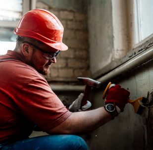 Professional worker, in uniform and safety helmet, getting rid from an old plaster at the brick wall